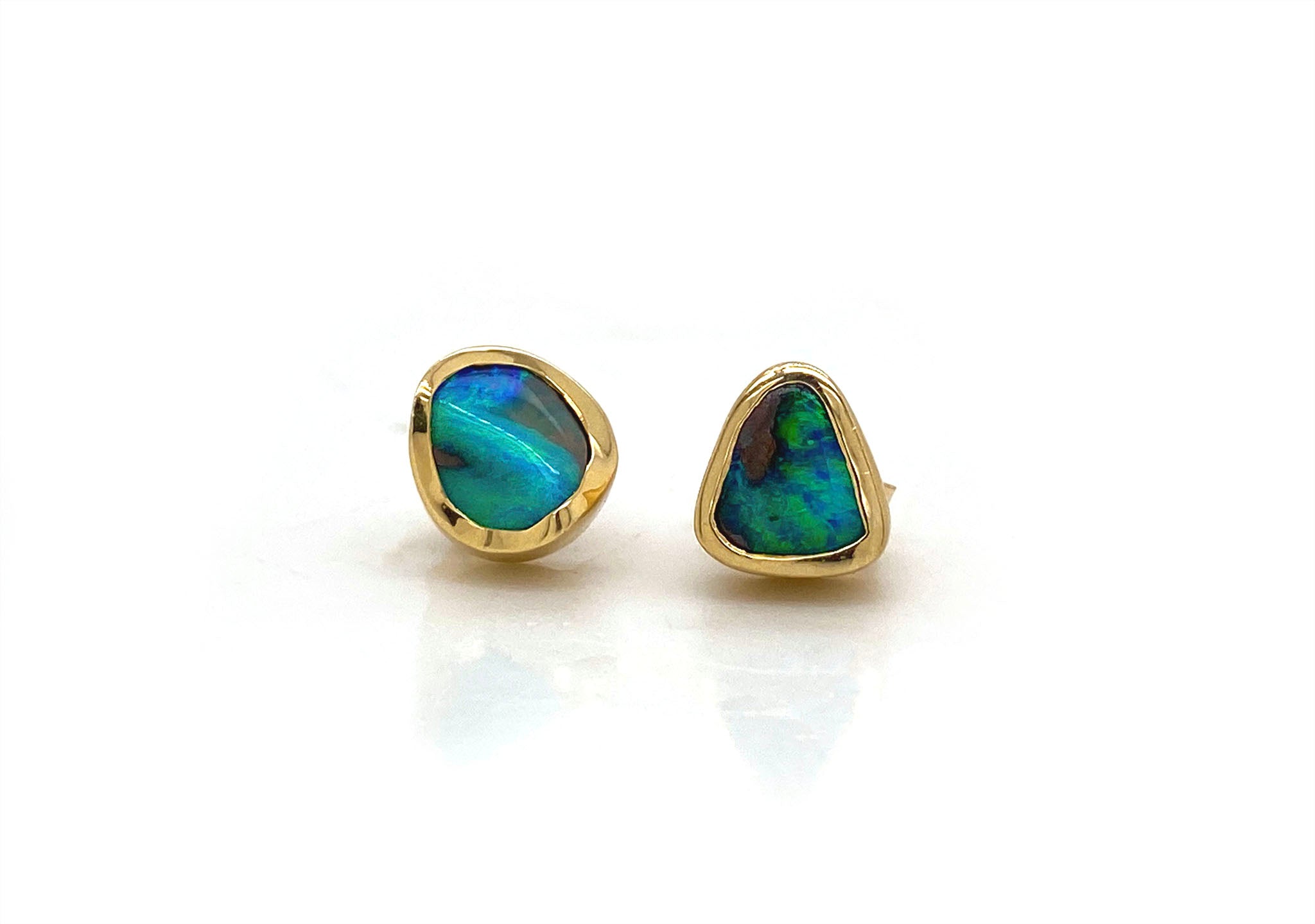 This remarkable pair of hand carved stud earrings showcases two natural Australian boulder opals with  vibrant flashes of oceanic blue and green. These exquisite gems are delicately wrapped in 18kt yellow gold with a luxurious satin finish. These opals are true works of art and will likely become a treasured family heirloom to be handed down form generation to generation.