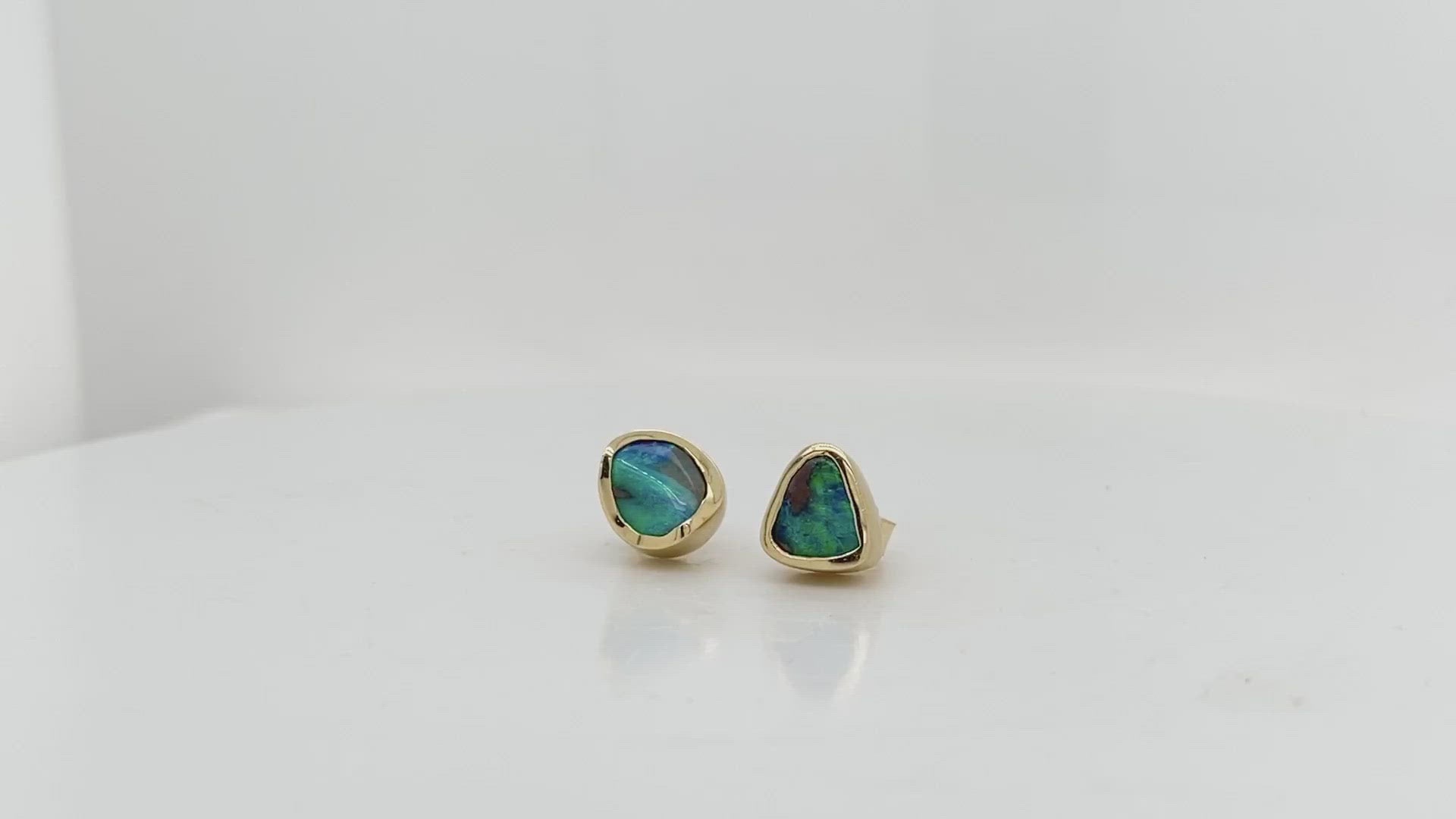 A Video- This remarkable pair of hand carved stud earrings showcases two natural Australian boulder opals with vibrant flashes of oceanic blue and green. These exquisite gems are delicately wrapped in 18kt yellow gold with a luxurious satin finish. These opals are true works of art and will likely become a treasured family heirloom to be handed down form generation to generation.