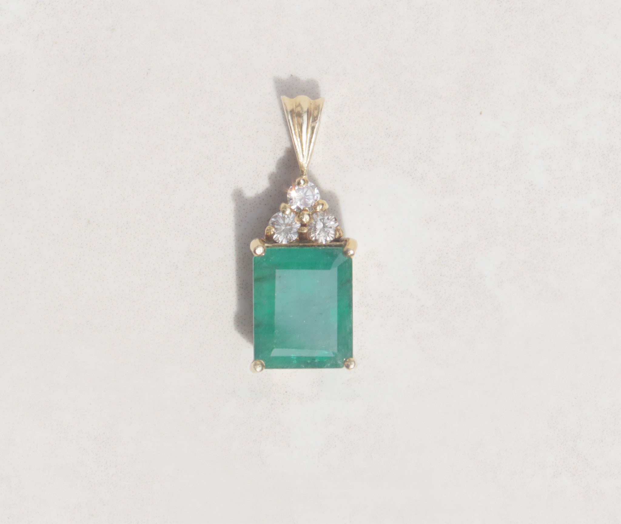 Simple but striking, this yellow gold pendant showcases a three carat Colombian emerald with three round brilliant cut diamonds.   Emerald is the birthstone for May  Emerald celebrates the twentieth and thirty-fifth wedding anniversaries