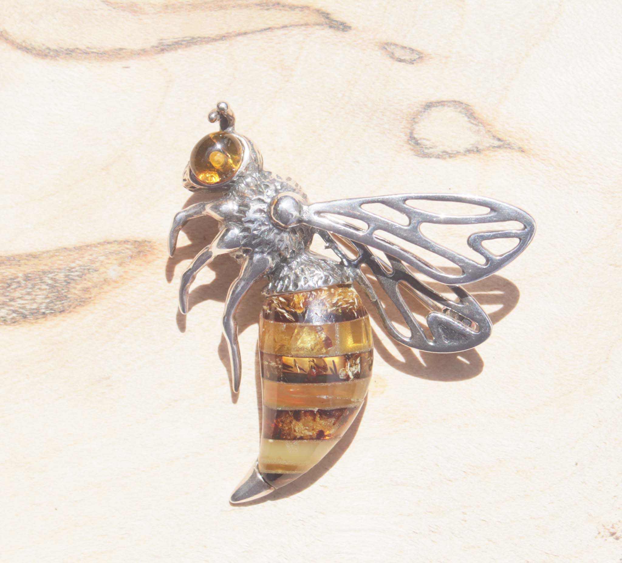 A captivating sterling silver queen bee brooch. Detailed with texture, this brooch features a beautiful variety of natural amber. Each amber slice contains an array of natural inclusions to reflect the interesting texture and colours of the queen bee's body. The sterling silver body has been oxidised and finished with a bright amber eye. Within the bee hive, the queen bee is said to be symbolic of femininity, motherhood empowerment and growth. This brooch will elevate both formal and everyday wear.