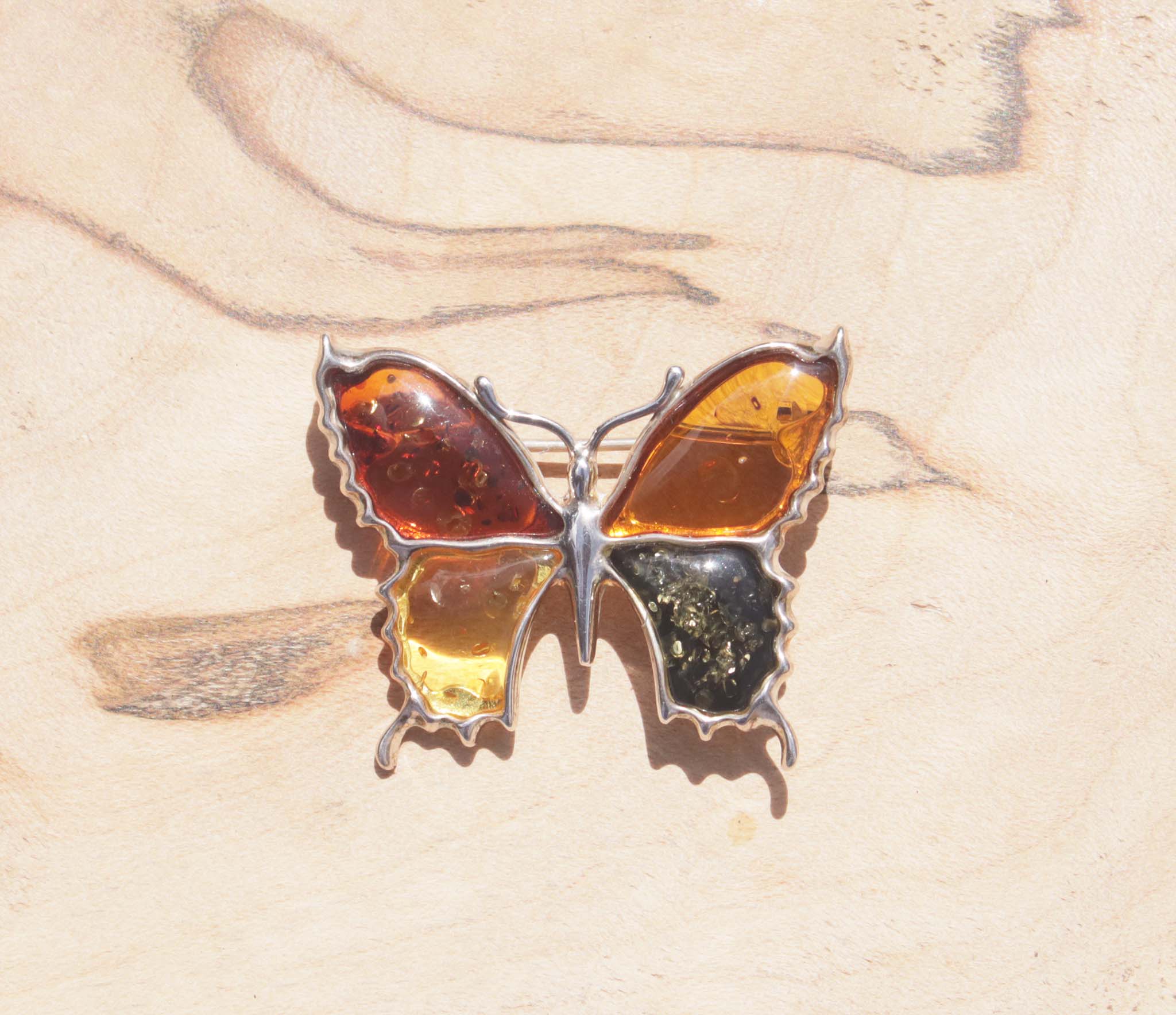 An eye-catching sterling silver amber butterfly brooch. This brooch contains a variety of natural amber, a natural material made from the resin of trees. Set in sterling silver, the amber wings include cognac, honey, orange and green amber.