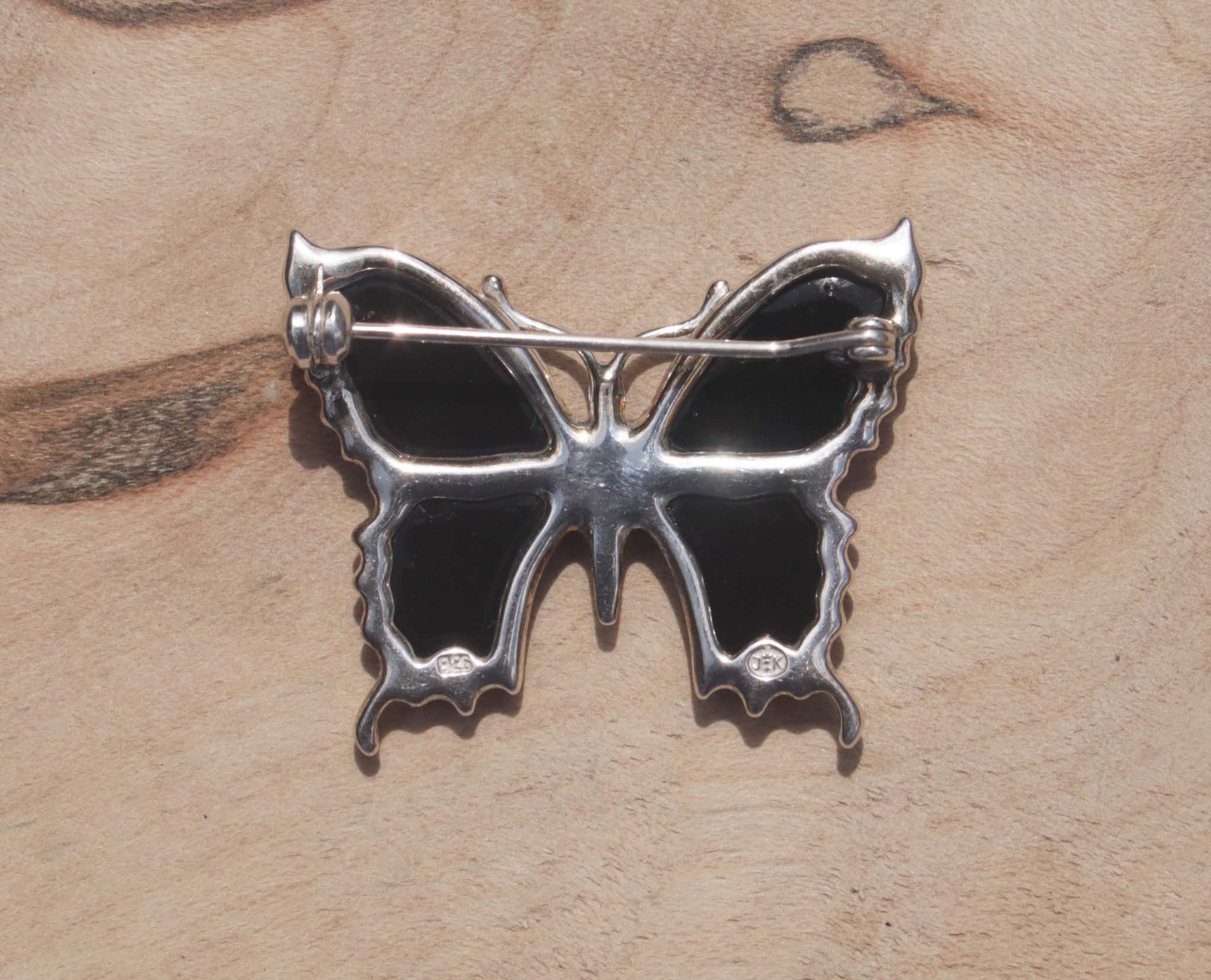 An eye-catching sterling silver green amber butterfly brooch. This brooch features green amber, a natural material made from the resin of trees. Set in sterling silver, this gorgeous brooch will dress your up everyday wear or add a note of elegance to formal wear. This image shows the back of the brooch with hallmarking