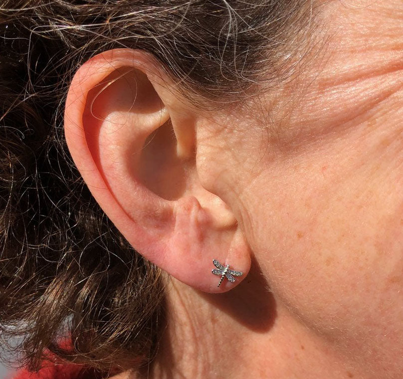 An dainty pair of pavé Dragonfly stud earrings. Made with nature lovers in mind, this pair of studs are perfect for everyday wear. This pair of earrings have gemstone filled wings with a detailed solid silver body. An image of a model wearing dragonfly studs.