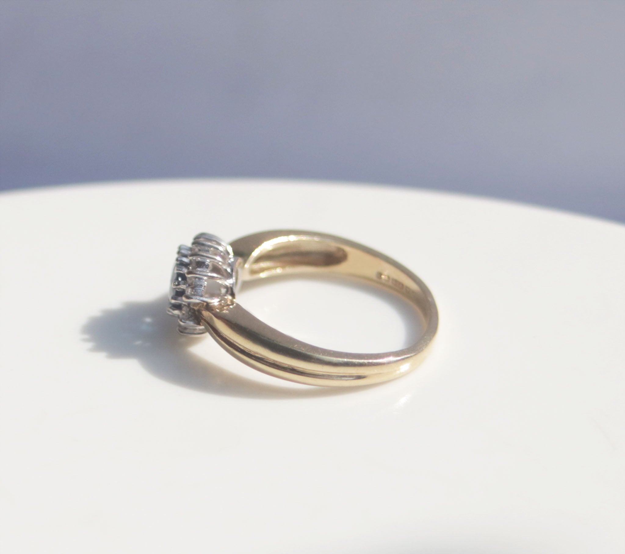 A classic Edwardian inspired sapphire and diamond ring. Crafted from 9ct yellow gold, this classic design features a vivid blue sapphire surrounded by fourteen round brilliant cut diamonds. With a carat weight of 0.75ct, the rich blue sapphire takes centre stage among a cluster of round brilliant diamonds