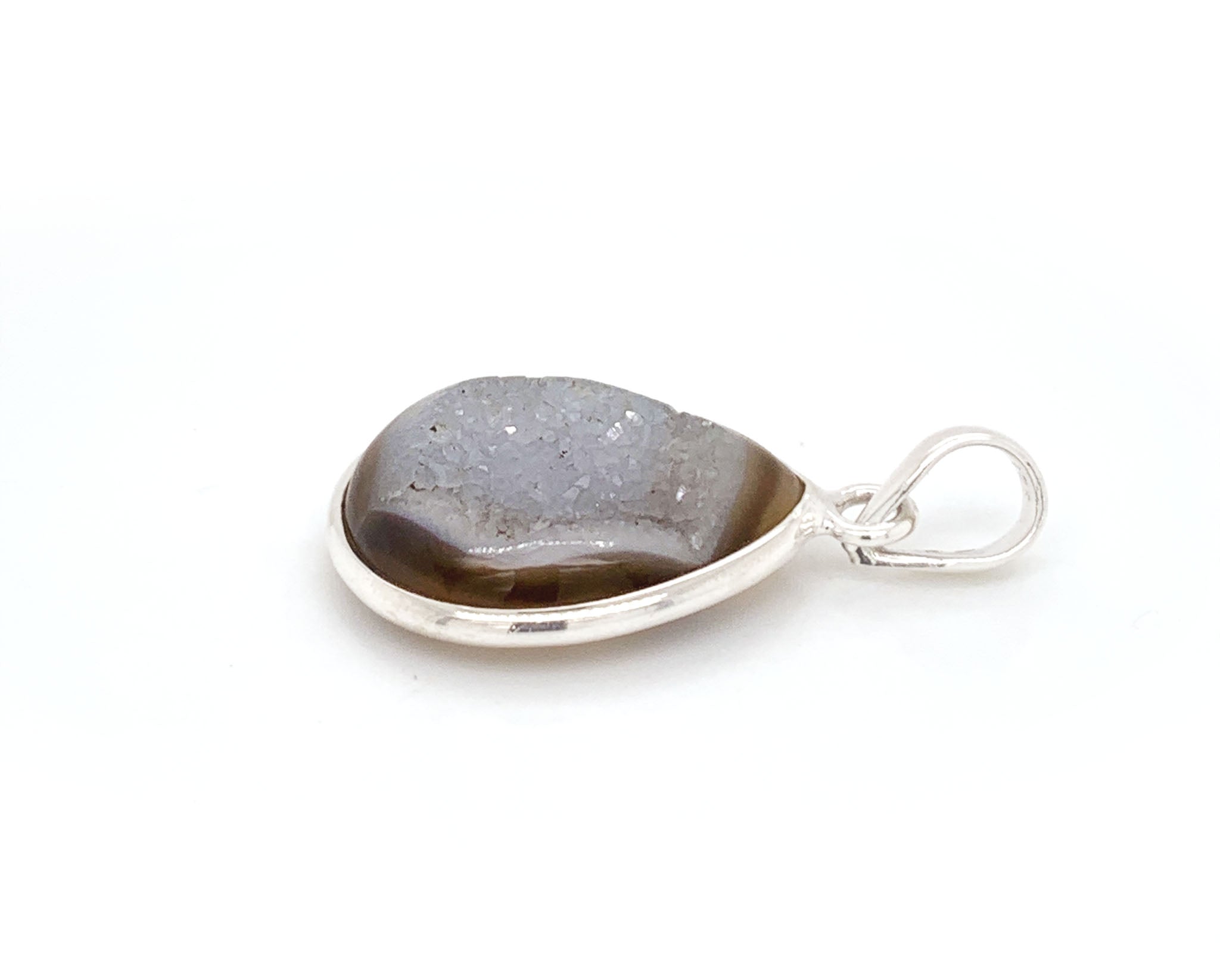 This sterling silver pendant features a Onyx, a variety of chalcedony and a member of the quartz family with a hexagonal crystal system. This gem stands out among others, due to the lustrous colony of crystals formed on its surface known as druzy. This special brown onyx has an visible band across on the top with a unique surface of crystals.