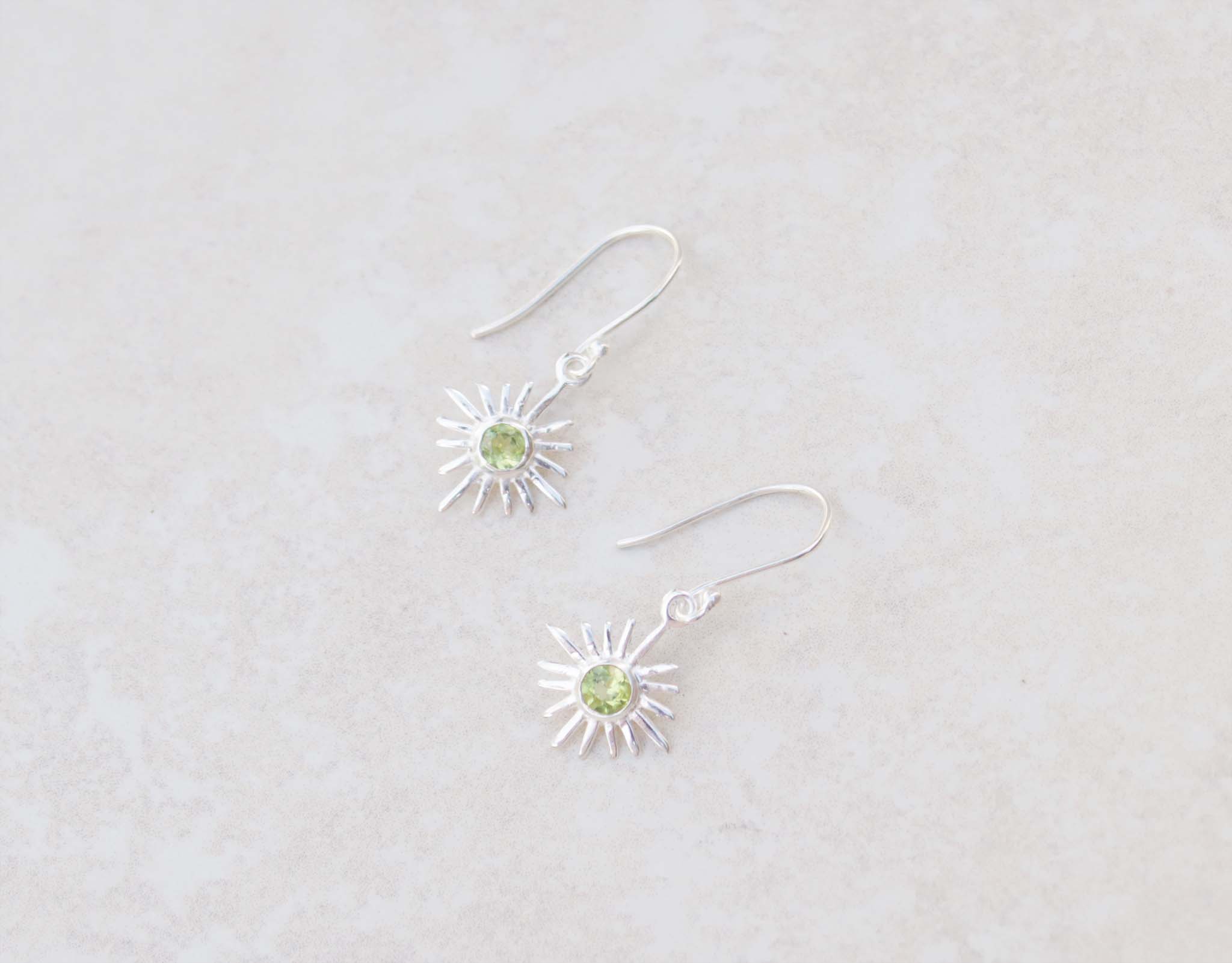 This pair of silver hook earrings feature a dainty star centered with peridot gems. The colour of the centre gem is bright green