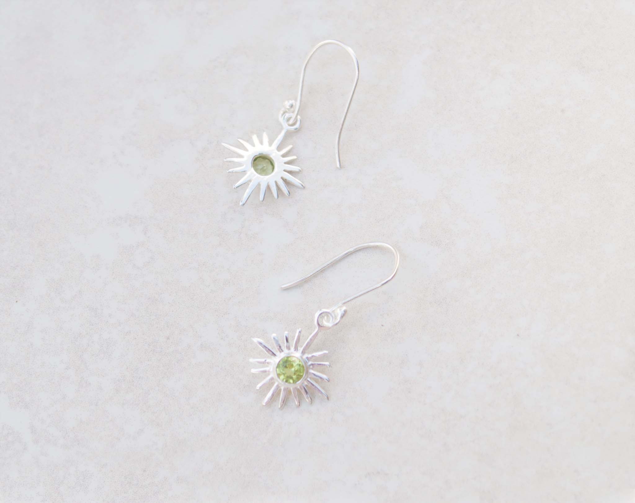 This pair of silver hook earrings feature a dainty star centered with peridot gems. The colour of the centre gem is bright green