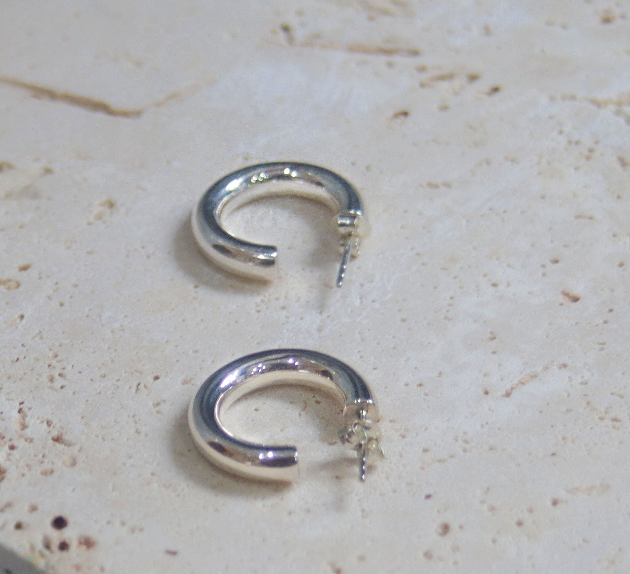 A stylish pair of silver hoop earrings .  These polished hinged hoops have a thick tubular body