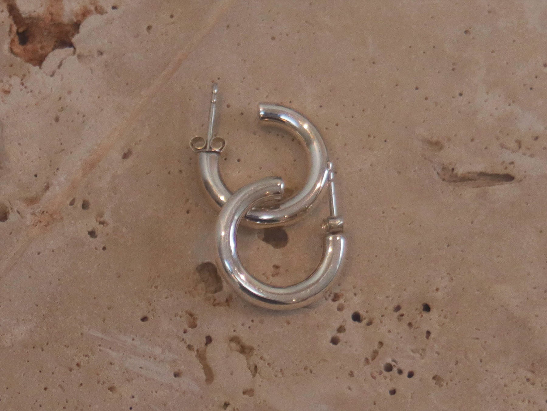 A stylish pair of silver hoop earrings . These polished hinged hoops have a thick tubular body