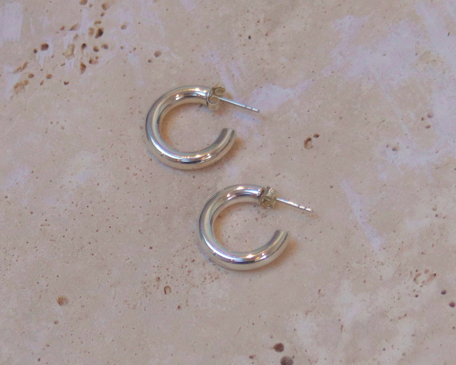A stylish pair of silver hoop earrings . These polished hinged hoops have a thick tubular body