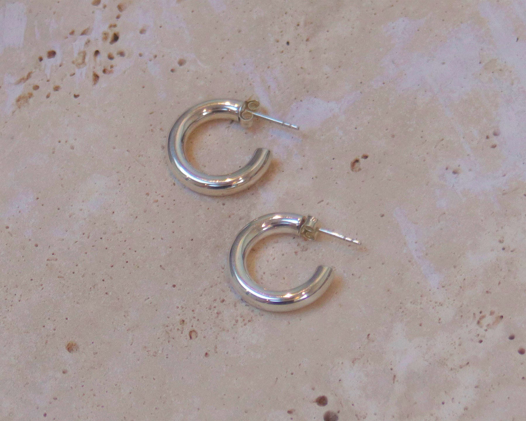 A stylish pair of silver hoop earrings .  These polished hinged hoops have a thick tubular body