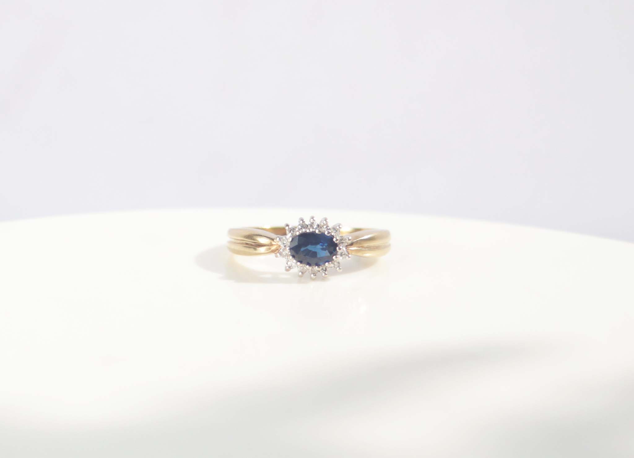 A classic Edwardian inspired sapphire and diamond ring. Crafted from 9ct yellow gold, this classic design features a vivid blue sapphire surrounded by fourteen round brilliant cut diamonds. With a carat weight of 0.75ct, the rich blue sapphire takes centre stage among a cluster of round brilliant diamonds.