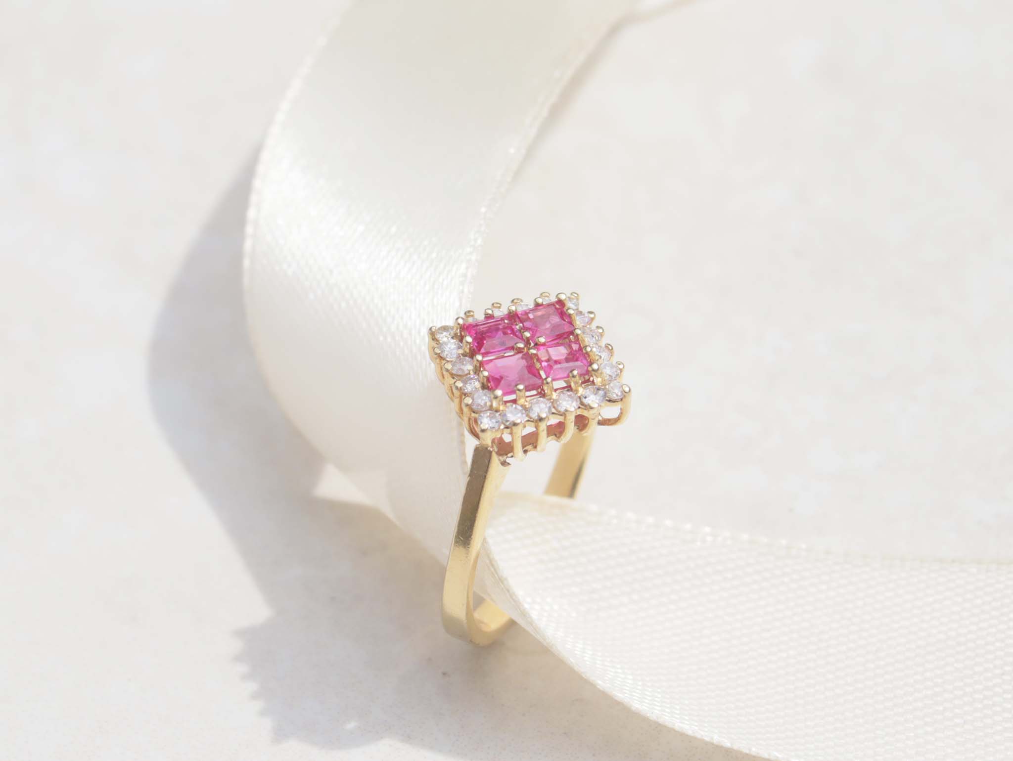 A ladies 18ct yellow gold ruby and diamond vintage ring. This gorgeous piece features four masterfully cut ruby gems. Each gem has a strong red-pink colour with a halo of round brilliant cut diamonds, with a total carat weight of 0.40cts.