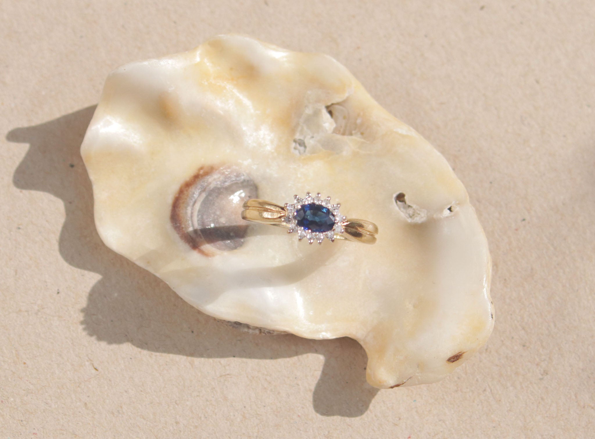 This classic design features a royal blue sapphire surrounded by a cluster of diamonds set in 9kt yellow gold band. The outer claw setting creates an elegant Edwardian aesthetic and makes this ring a real sparkling showstopper.