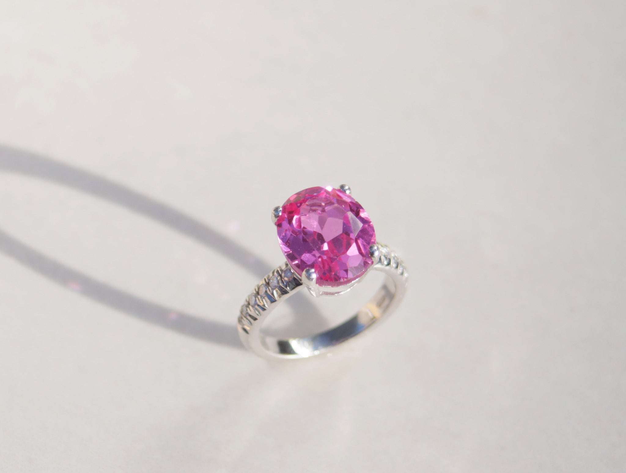 This captivating ring features an oval cut pink topaz set in four claws, which mirrors light throughout. The white gold band features twelve round cut diamonds with a total carat weight of cts.
