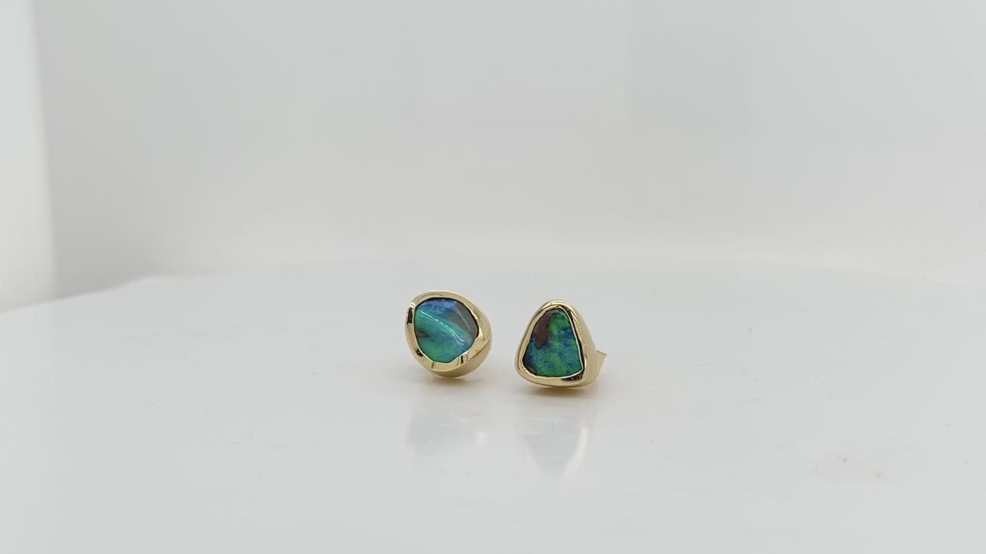 A Video- This remarkable pair of hand carved stud earrings showcases two natural Australian boulder opals with  vibrant flashes of oceanic blue and green. These exquisite gems are delicately wrapped in 18kt yellow gold with a luxurious satin finish. These opals are true works of art and will likely become a treasured family heirloom to be handed down form generation to generation. 