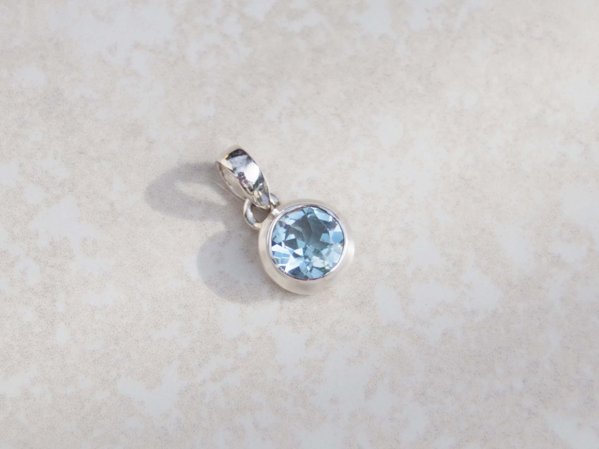 This round pendant features an aquamarine and sterling silver. Dressed with a dainty silver chain, this gem stands out for its vivid sky blue colour and brilliance. 