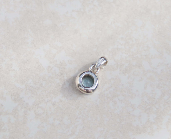 This round pendant features an aquamarine and sterling silver. Dressed with a dainty silver chain, this gem stands out for its vivid sky blue colour and brilliance. 