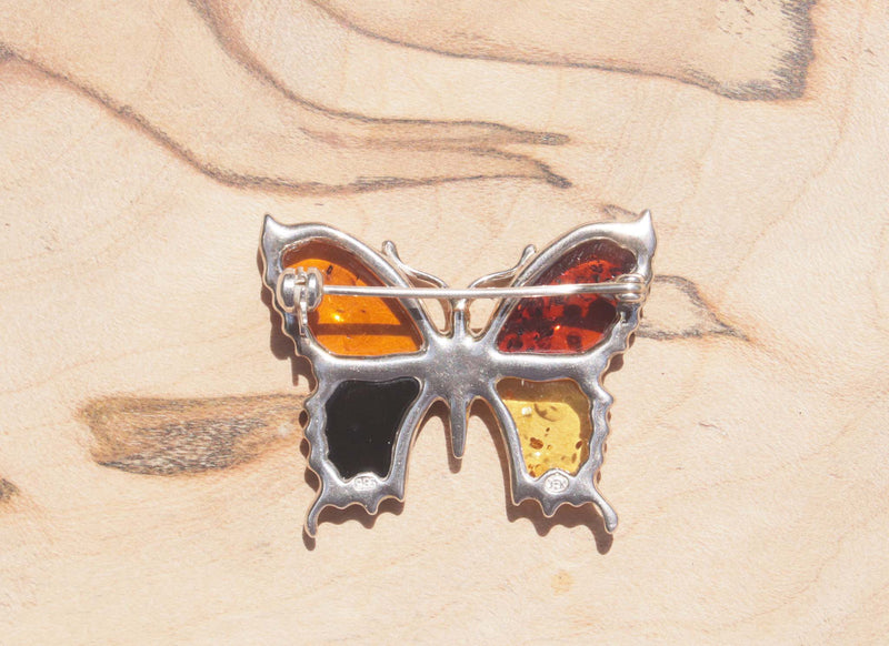 An eye-catching sterling silver amber butterfly brooch.   This brooch contains a variety of natural amber, a natural material made from the resin of trees. Set in sterling silver, the amber wings include cognac, honey, orange and green amber.  This image shows the back of the brooch.