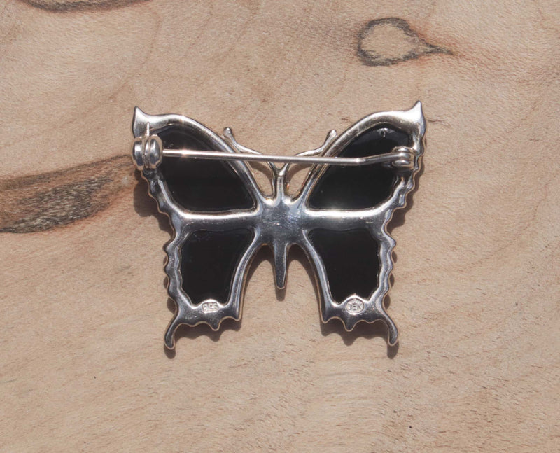 An eye-catching sterling silver green amber butterfly brooch.   This brooch features green amber, a natural material made from the resin of trees. Set in sterling silver, this gorgeous brooch will dress your up everyday wear or add a note of elegance to formal wear.  This image shows the back of the brooch with  hallmarking 