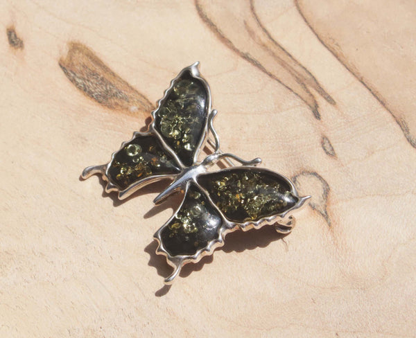 An eye-catching sterling silver green amber butterfly brooch.   This brooch features green amber, a natural material made from the resin of trees. Set in sterling silver, this gorgeous brooch will dress your up everyday wear or add a note of elegance to formal wear. 