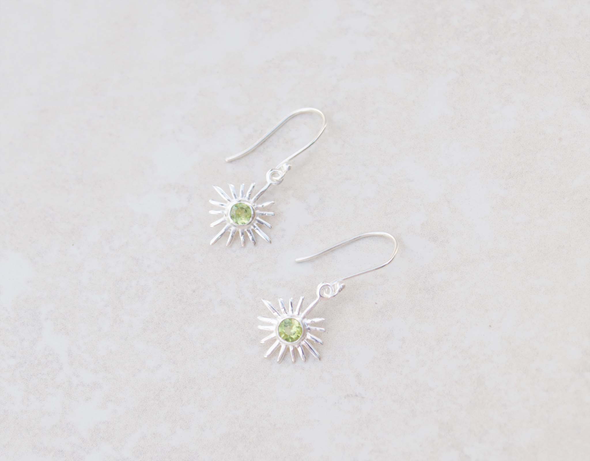 This pair of silver hook earrings feature a dainty star centered with peridot gems. The colour of the centre gem is bright green 