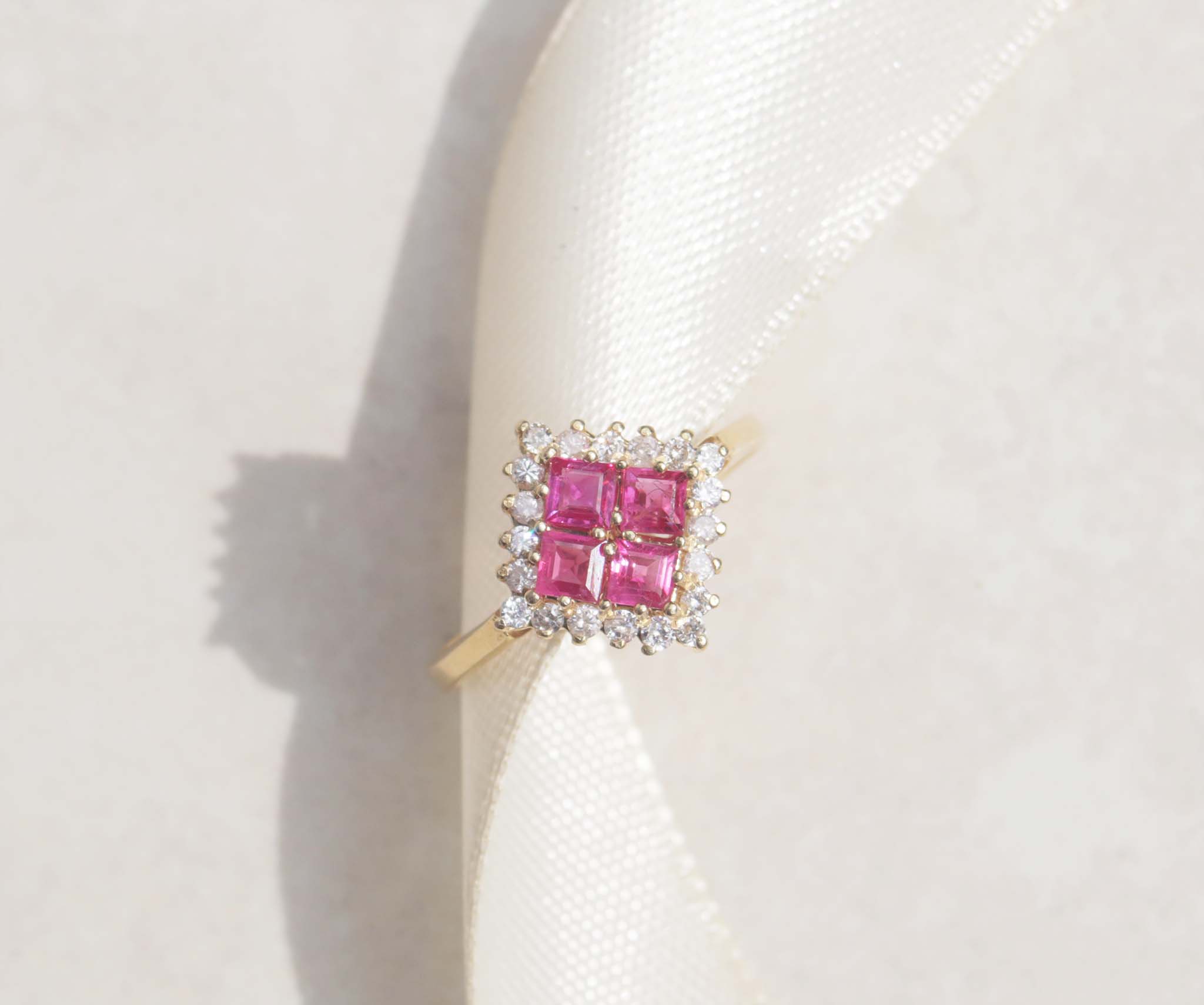 A ladies 18ct yellow gold ruby and diamond vintage ring. This gorgeous piece features four masterfully cut ruby gems. Each gem has a strong red-pink colour with a halo of round brilliant cut diamonds, with a total carat weight of 0.40cts. 