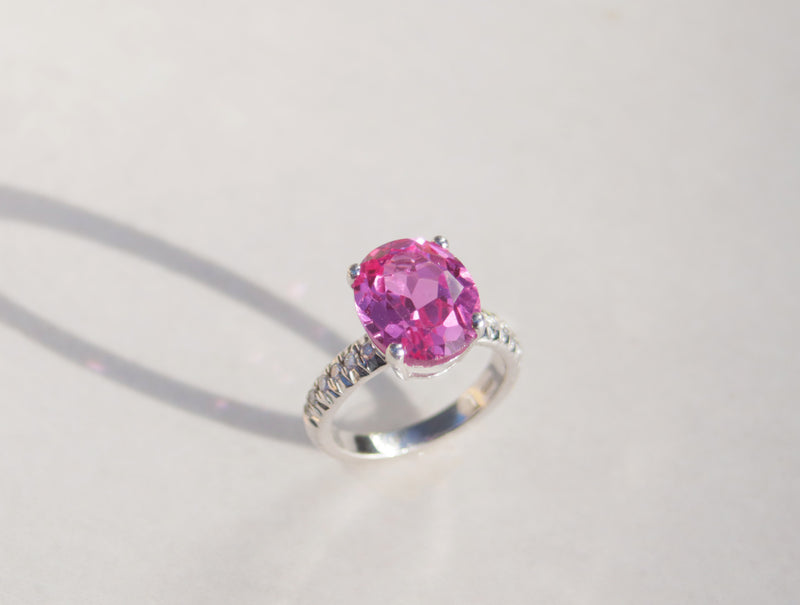 This captivating ring features an oval cut pink topaz set in four claws, which mirrors light throughout. The white gold band features twelve round cut diamonds with a total carat weight of cts. 